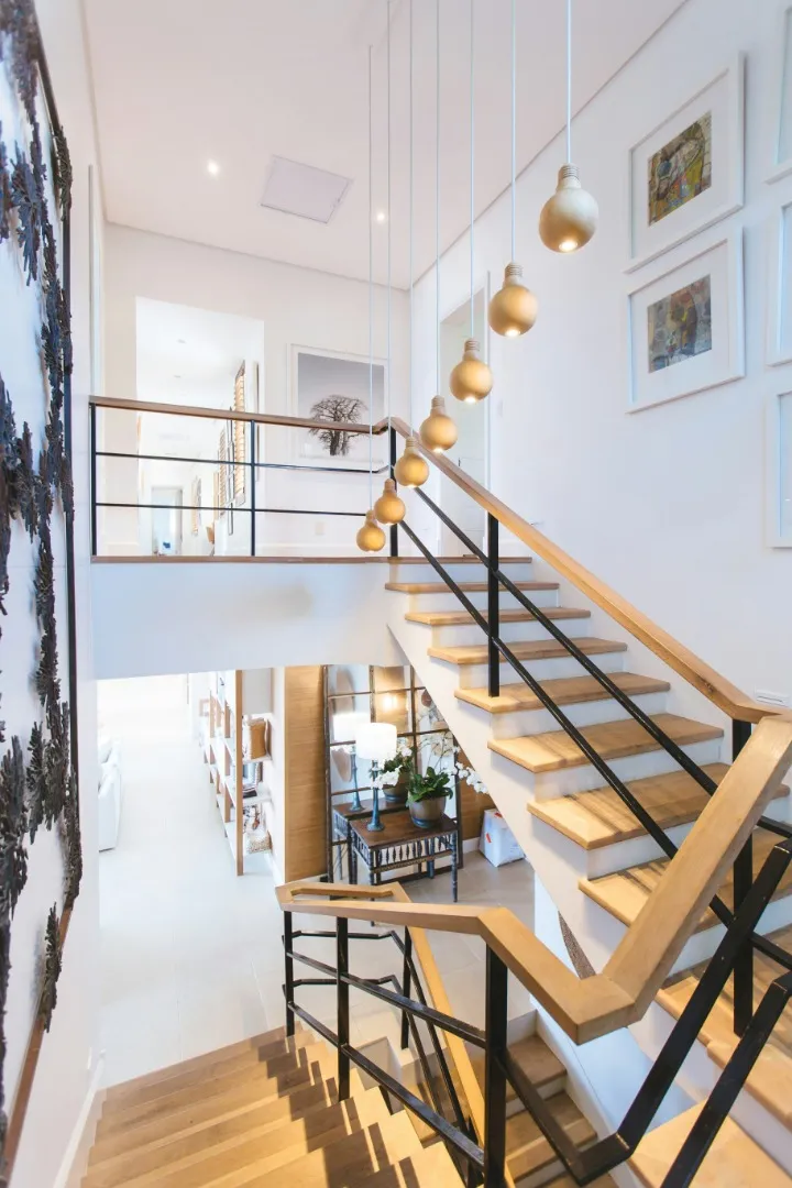 Bright two-story stair hall with a wood staircase, a cluster of pendant bulbs and a single console table holding a white orchid, one healthy plant giving scale to a tight footprint in a listed New Jersey townhouse