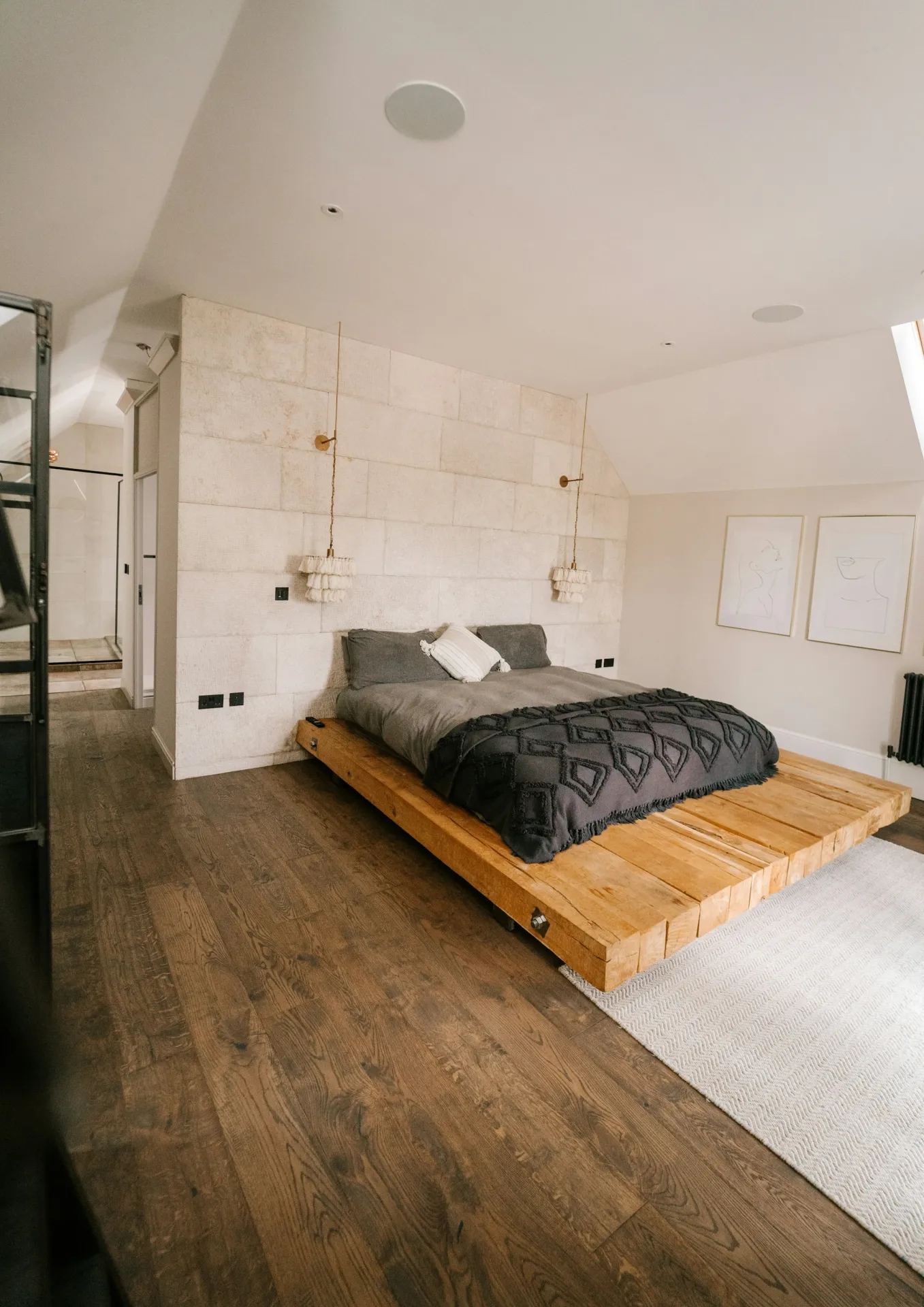 Bedroom with a low platform bed made with gray sheets and a dark tufted throw, a chunky woven rug on a dark wood floor and fringed pendant lights, the kind of bedding, blanket and rug that hold a pet’s smell long after the pet has left the room